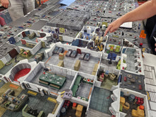 Load image into Gallery viewer, A detailed tabletop display of a miniature sci-fi city or building set, with rooms, corridors, vehicles, and small figures visible. A person's arm and hand are pointing at the model from above.